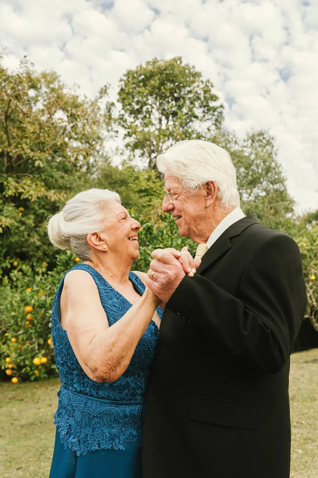 An older couple dancing on the lawn, laughing, his hand holding hers.