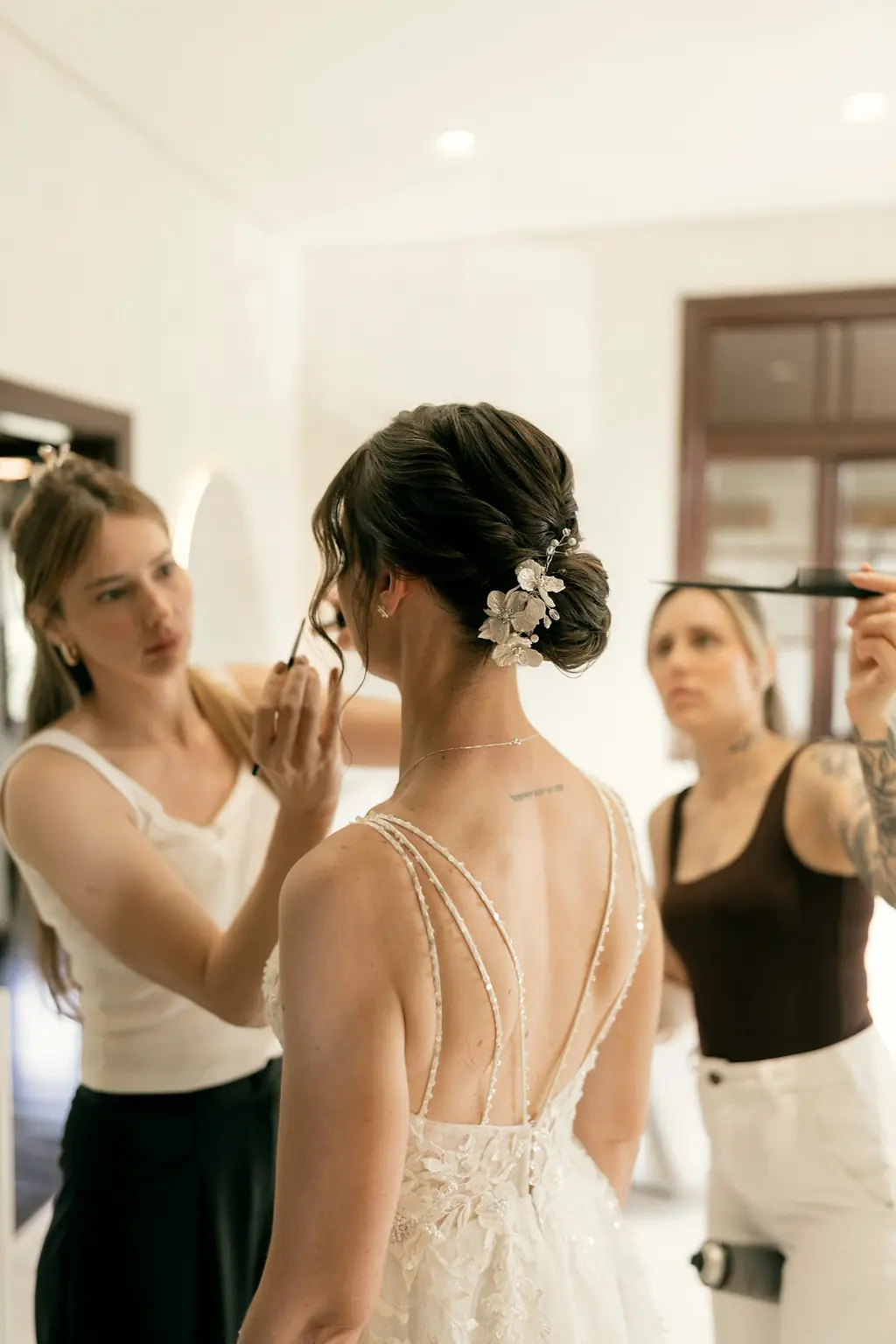 Two friends doing the bride's make-up and hair in a white room.